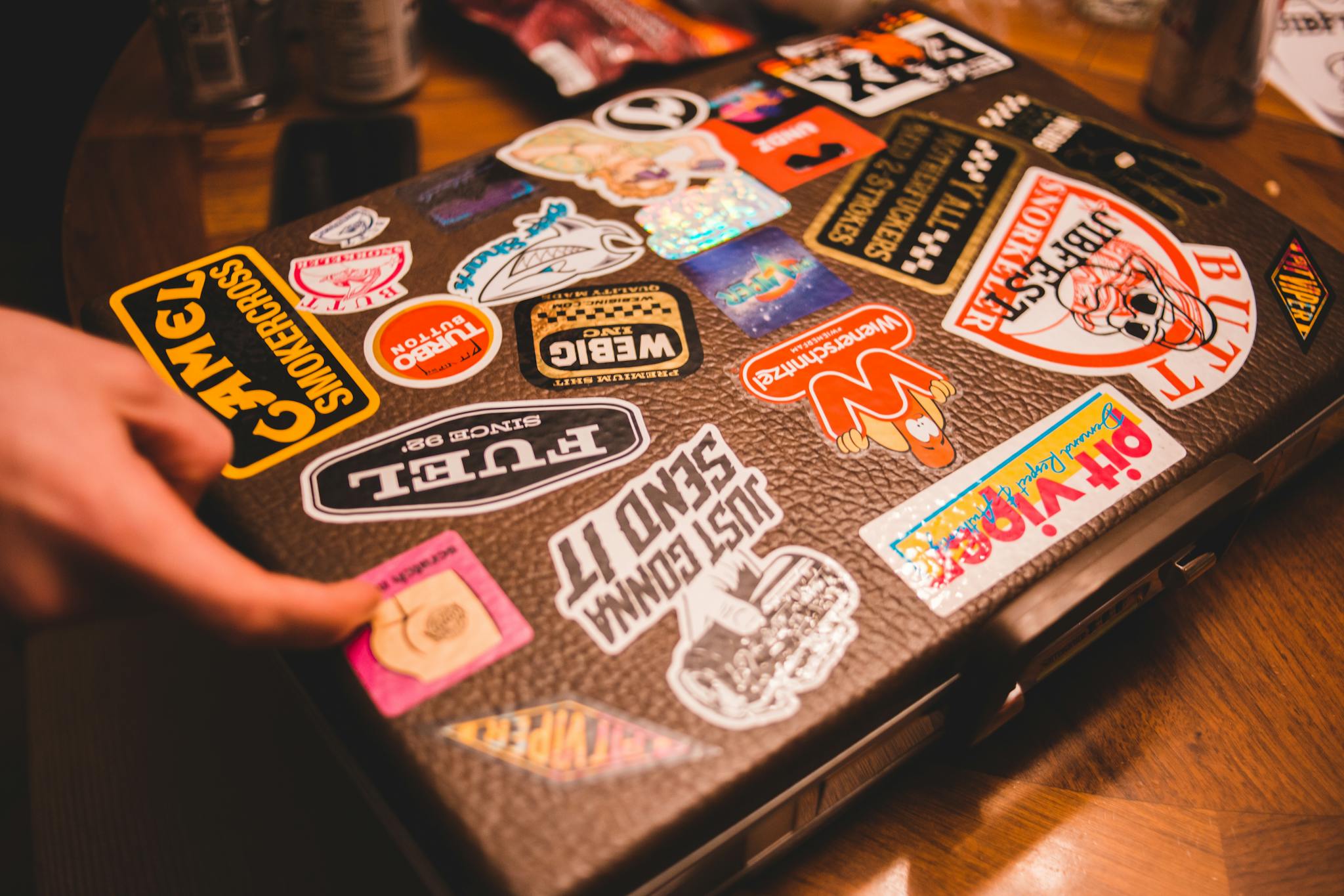 A suitcase covered with various colorful stickers on a wooden table indoors.