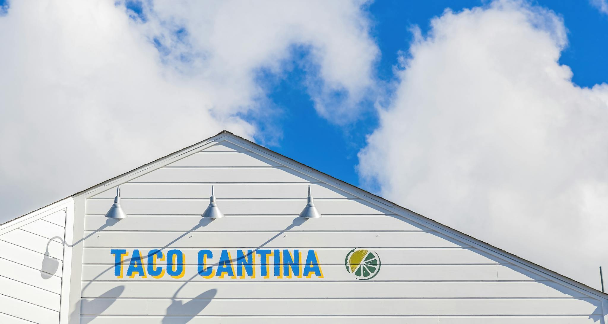 Taco Cantina sign on a white building with a bright blue sky backdrop.